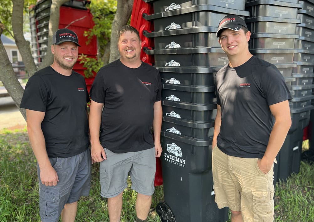 Three men standing in front of a pile of trash cans.