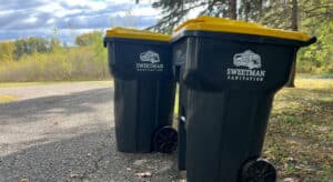 Two yellow and black trash cans on a road.