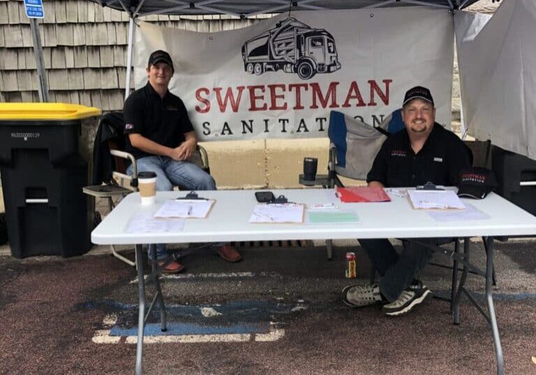 Two men sitting at a table under a tent.